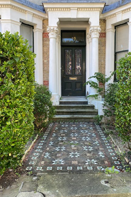 The image features the entrance to a traditional terraced house with a black front door framed by white decorative columns and intricate detailing above the doorway. A small flight of three stone step